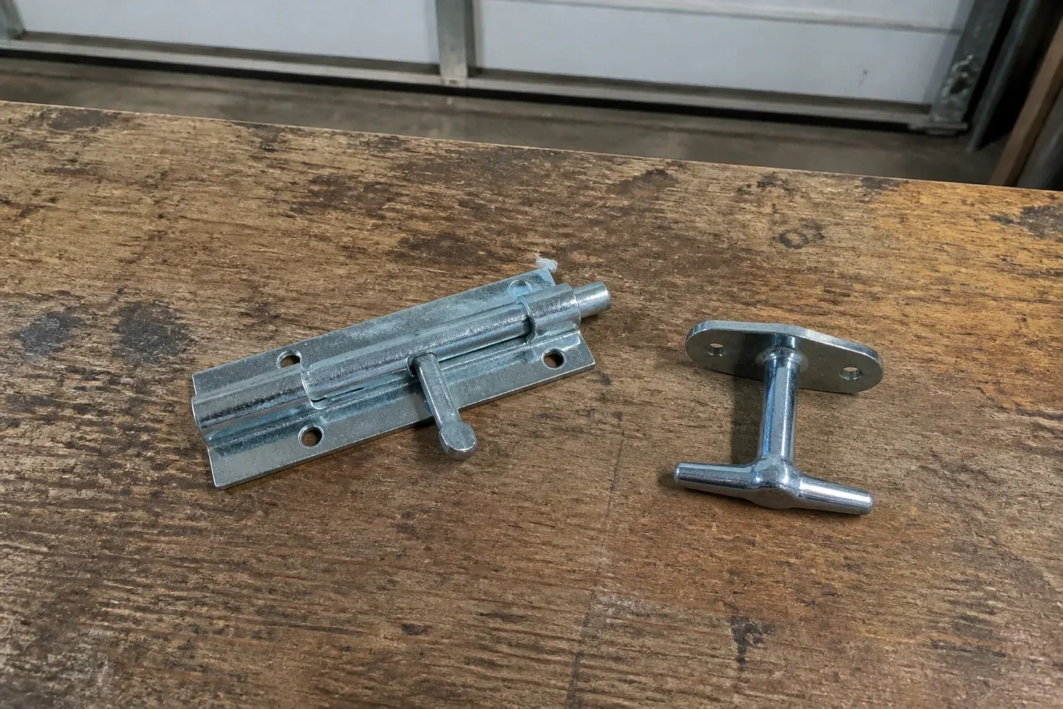 Detached slide bolt and T-handle on a wooden garage workbench. — Garage Door Manual Lock Repair, Woodstock