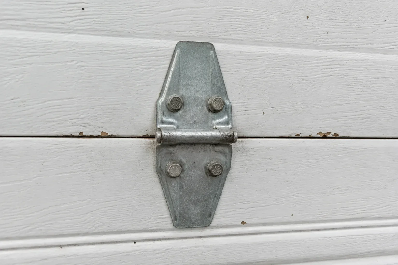 Metal center hinge across a seam in a white sectional garage door. — Garage Door Hinge Replacement, Woodstock